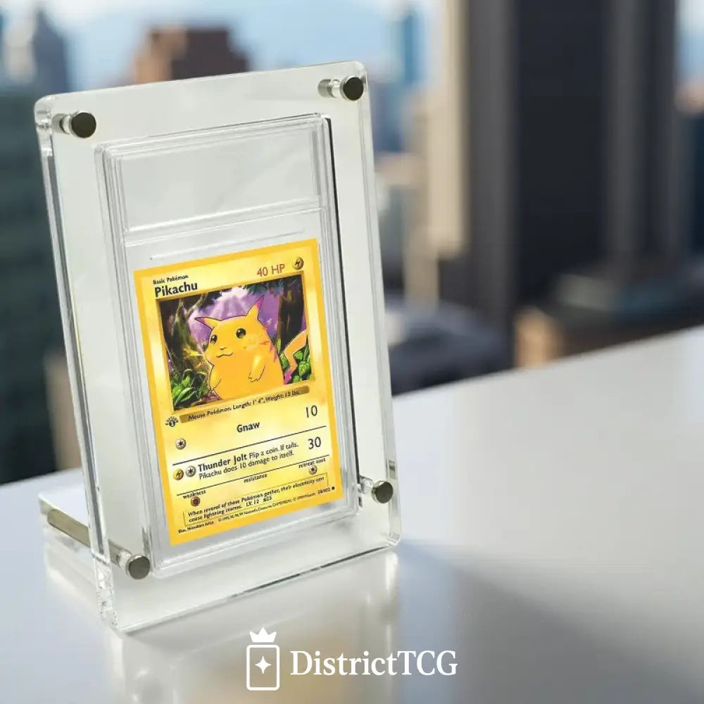 Présentoir en acrylique ultra clair EVORETRO avec une carte Pokémon Pikachu exposée, posé sur une table avec vue sur des immeubles en arrière-plan.