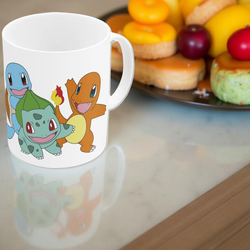 Mug Pokémon avec illustrations de Bulbizarre, Salamèche et Carapuce, posé sur une table à côté d'une assiette de pâtisseries colorées.