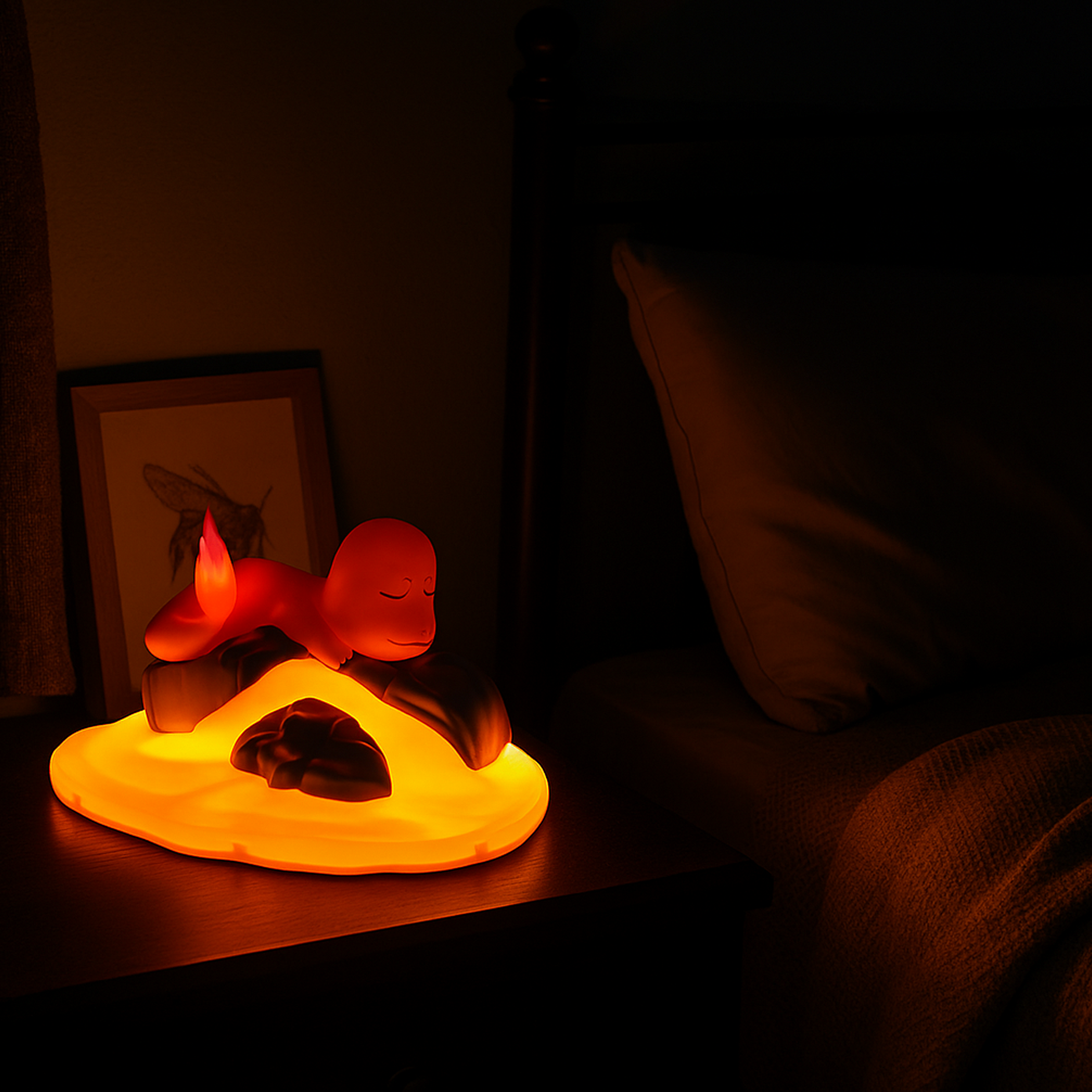 Lampe LED Pokémon Salamèche endormi sur un rocher de lave, utilisée comme veilleuse sur une table de chevet à côté d’un lit, ambiance de nuit chaleureuse.